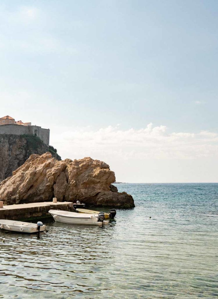 Fort Lovrijenac rising above an empty rocky cove outside Dubrovnik's Old Town walls with fishing boats moored in calm water