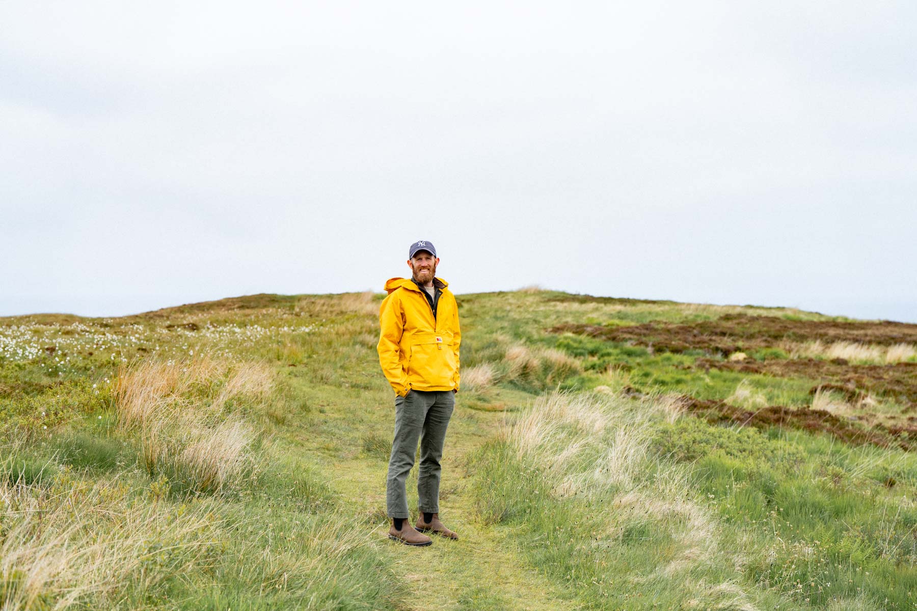 An empty single-track road curving through open green Highland moorland under a soft grey Scottish sky